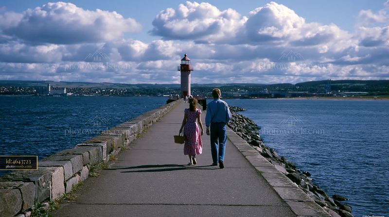 Couple walking near lighthouse on rocky path by the coast