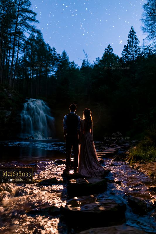 Couple under stars near a waterfall at night by the river