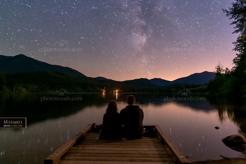 Couple sits by a mountain lake under a starry sky