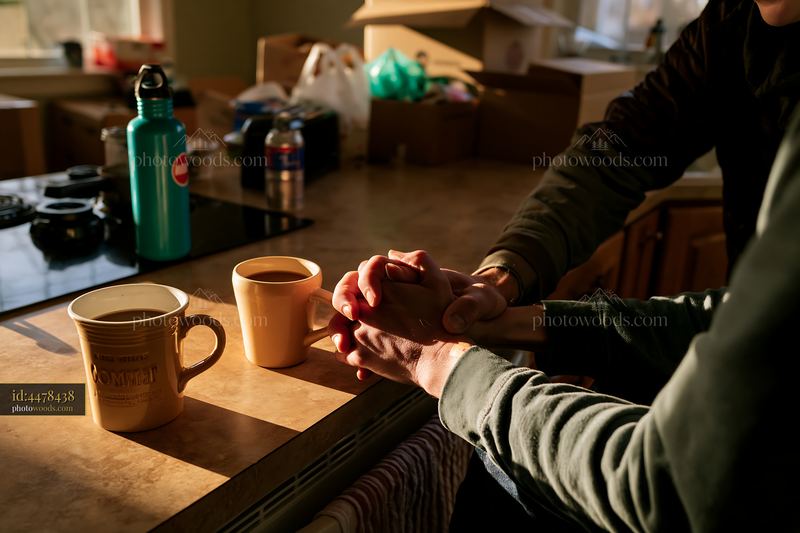 Two coffee cups beside intertwined hands on a kitchen table