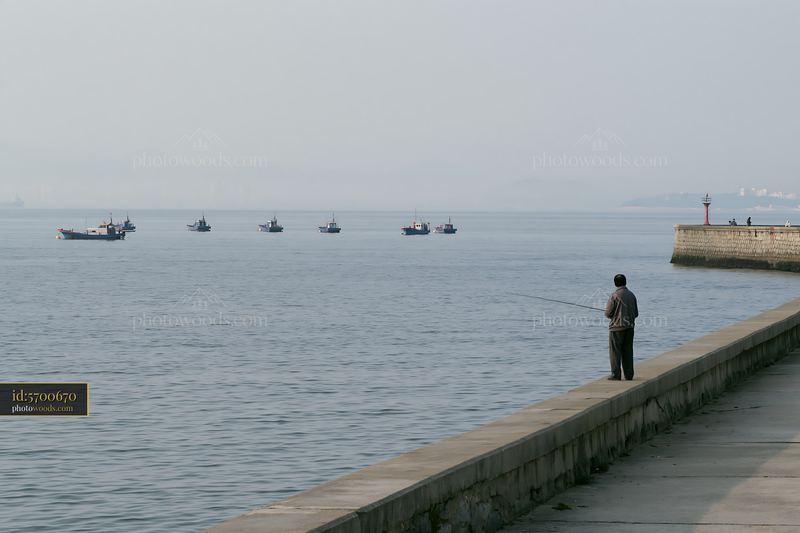 Fisherman by the water with boats in the background