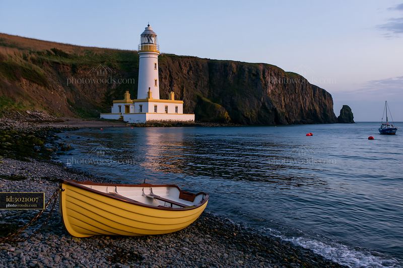 Lighthouse with boats in the foreground at sunset