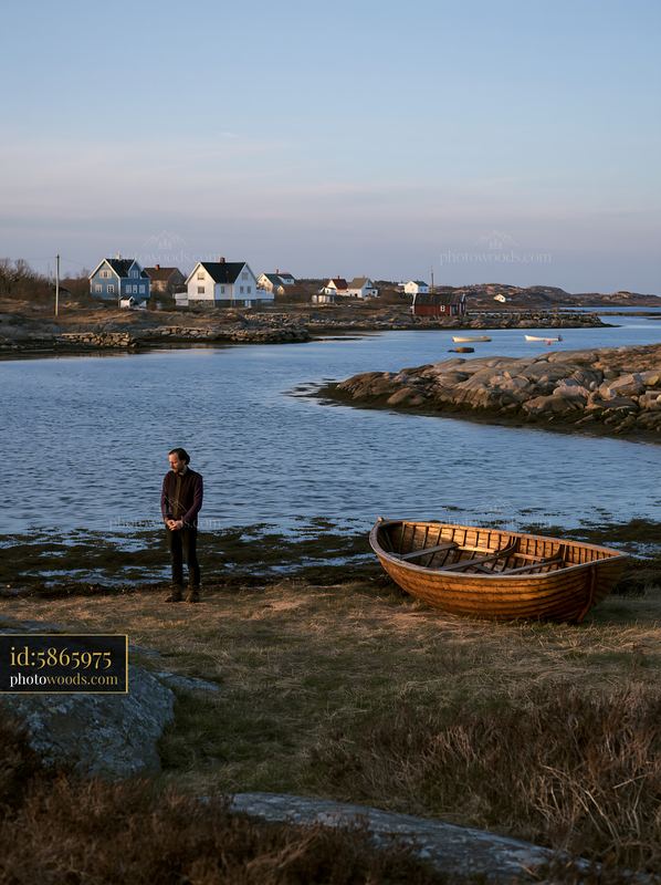 Coastline with lone person near wooden boat and houses