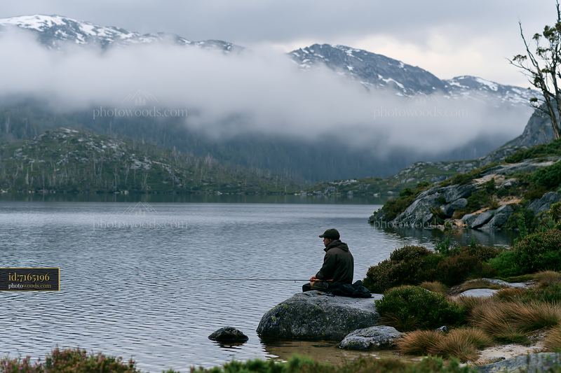 Fishing by an alpine lake beneath cloud-covered peaks