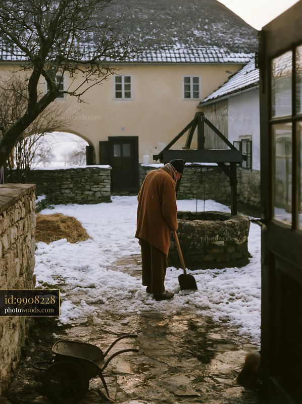 Farmhouse courtyard with well and person shoveling snow