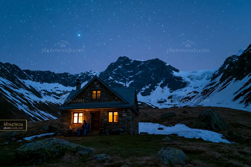 Photographer under stars in the mountains with a cabin
