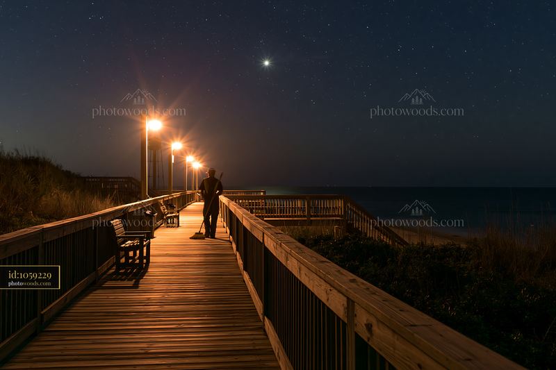 Starry night over a coastal boardwalk with a person standing