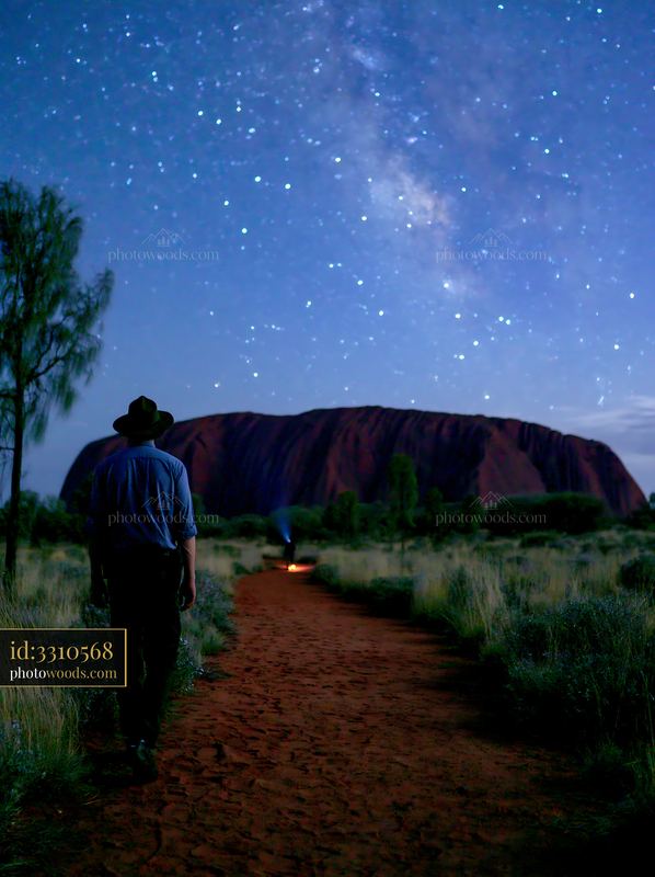 Uluru under a starry night sky with a person walking towards it