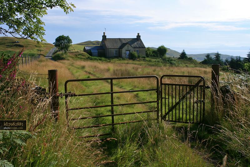 Rural cottage viewed through gate in a grassy landscape