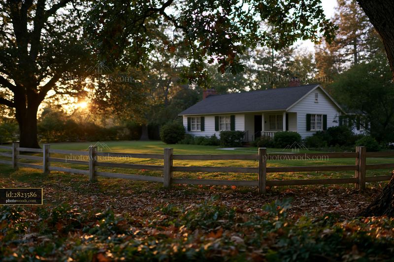 Rural home under oak trees with a wooden fence at sunset
