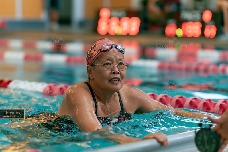 Senior woman swimming freestyle in lap pool with timer