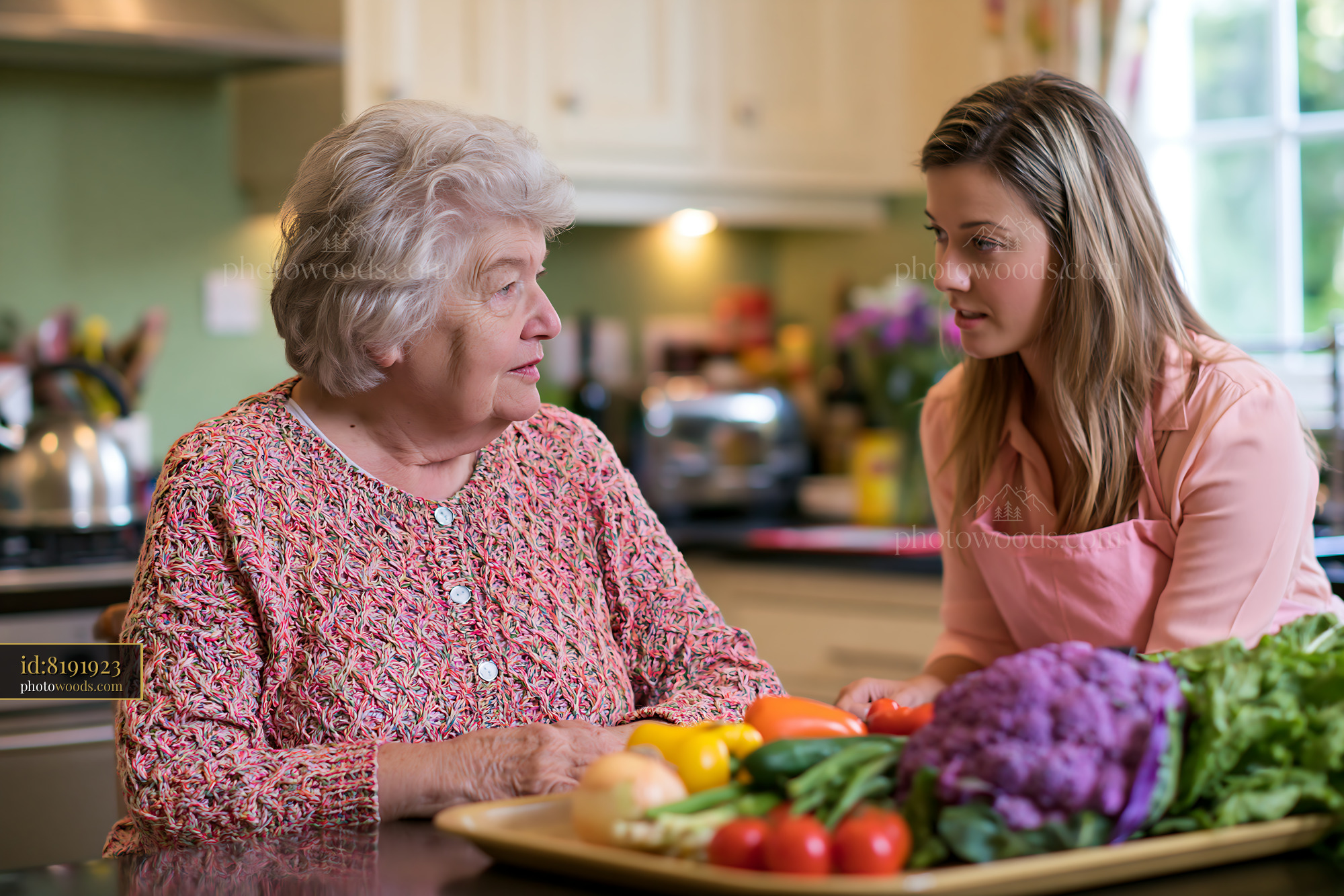 A senior woman with dementia is listening to a caregiver in a bright kitchen.