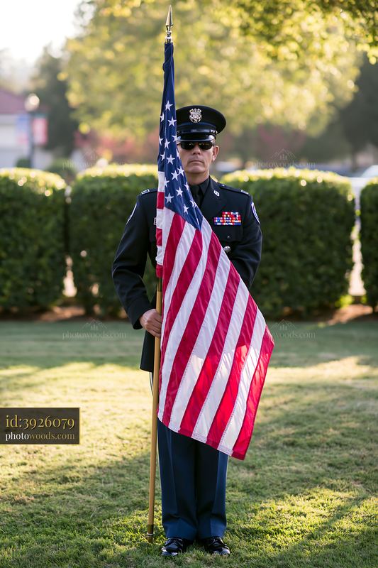 Sergeant stands at attention holding American flag in the park