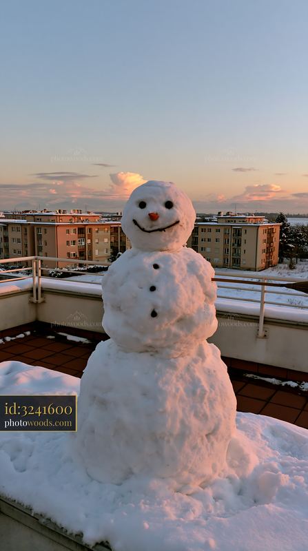 Snowman with a broomstick arm standing on a terrace at sunset