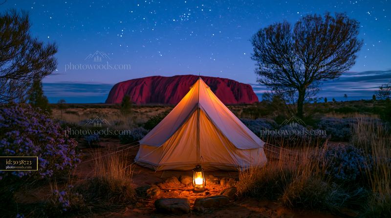 Uluru under a starry night sky with a tent and lantern
