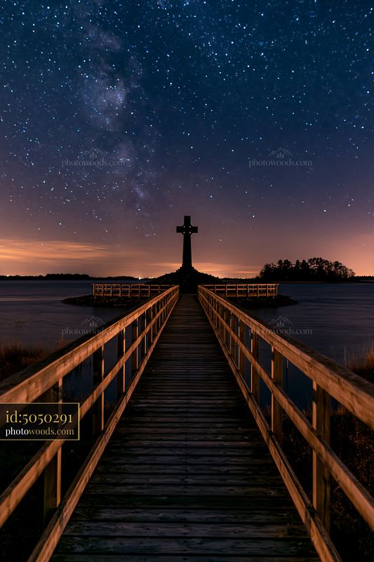 War memorial cross silhouetted against stars over wooden walkway