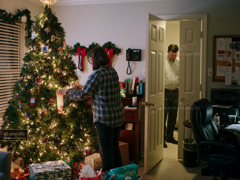 Parents placing gifts under tree in festive living room