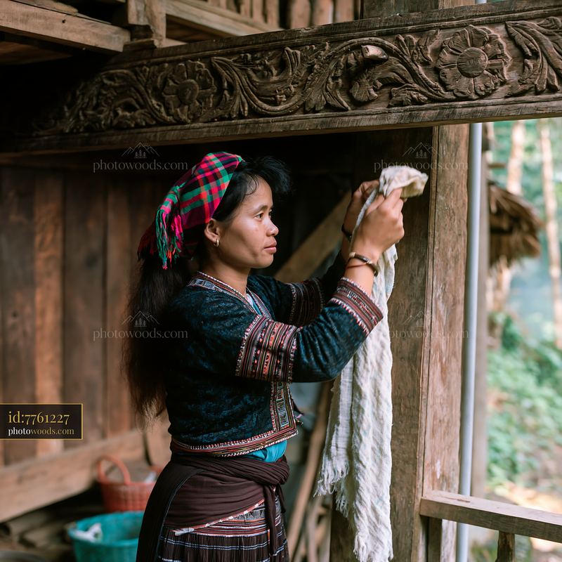 Woman in heritage attire cleaning wooden house decorations