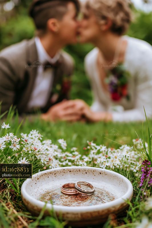 Couple kissing beside wedding rings in a flower-filled garden