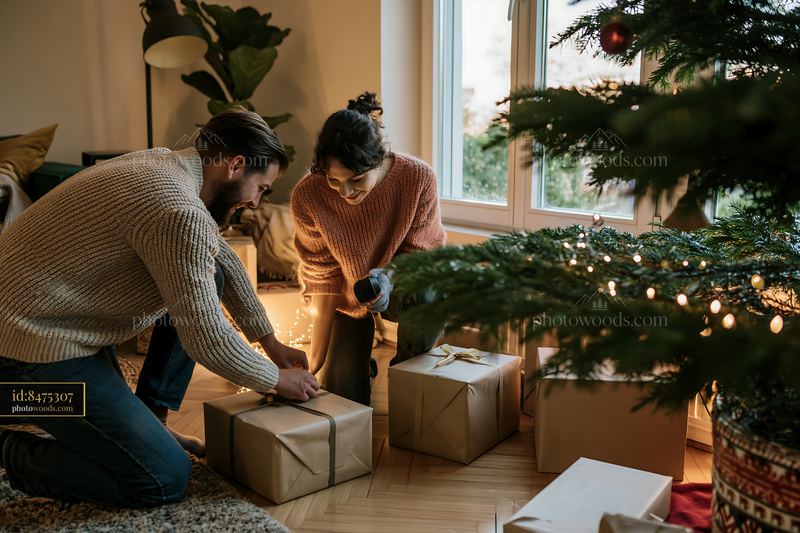 Couple placing wrapped gifts beneath a decorated Christmas tree