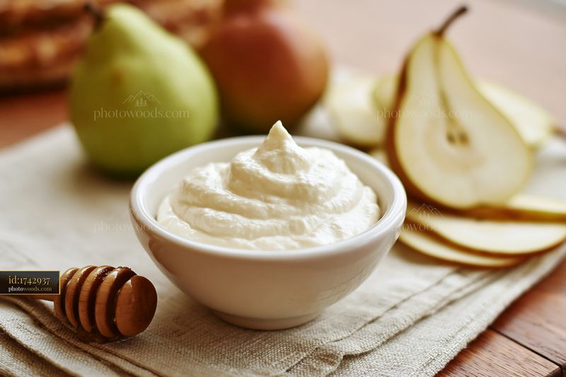 Cream dose beside honey dipper and sliced pears on a table