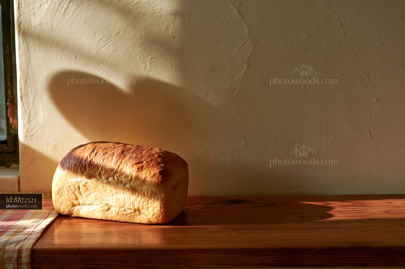 Fresh loaf with heart-shaped window-light shadow on rustic table