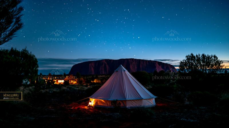 Uluru and illuminated tent beneath a starry night sky