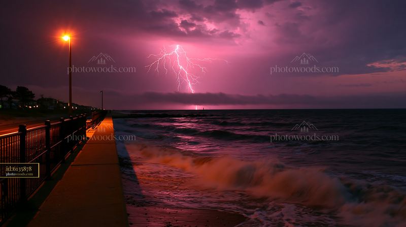 Coastline lit by lightning above ocean waves at night