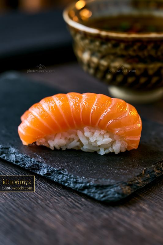 Salmon nigiri served on a slate plate with soy sauce in background