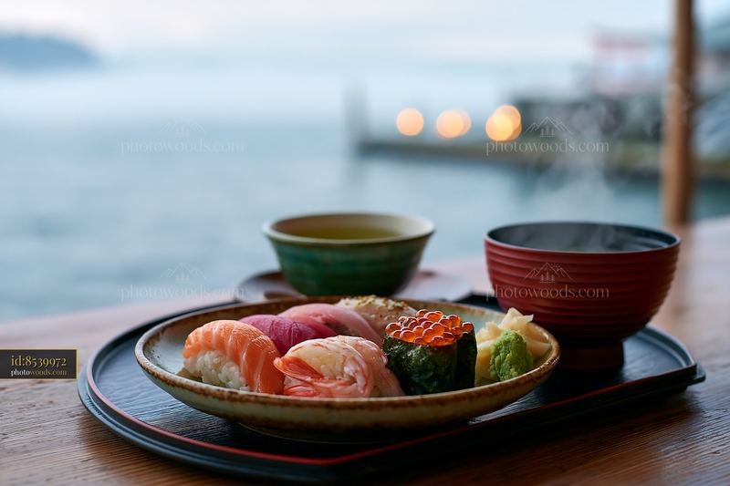 Sushi beside steaming green tea on a wooden table