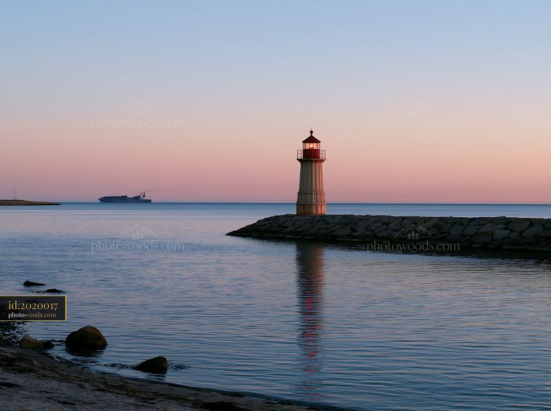 Lighthouse with a cargo ship in the distance at sunset