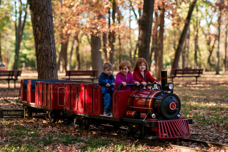 Three children riding a miniature train through an autumn park
