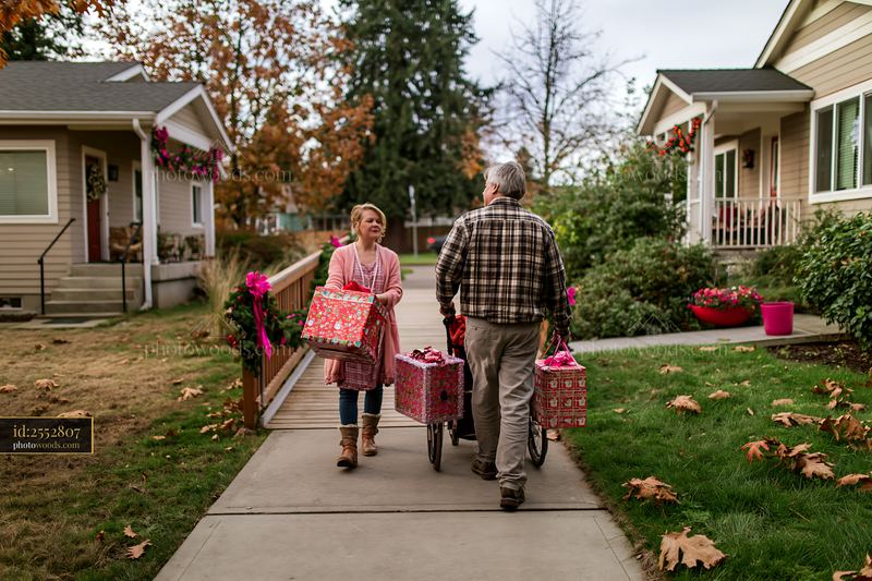 Parents Carrying Decorated Gift Boxes Through a Residential Walkway