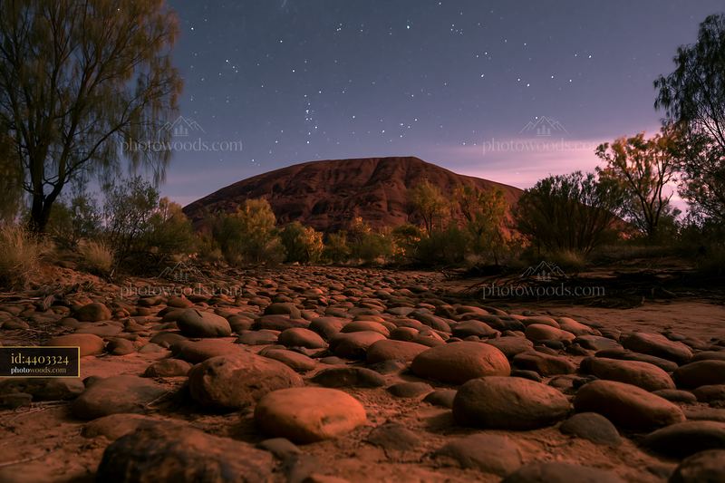 Uluru under a starry night sky with rocky foreground