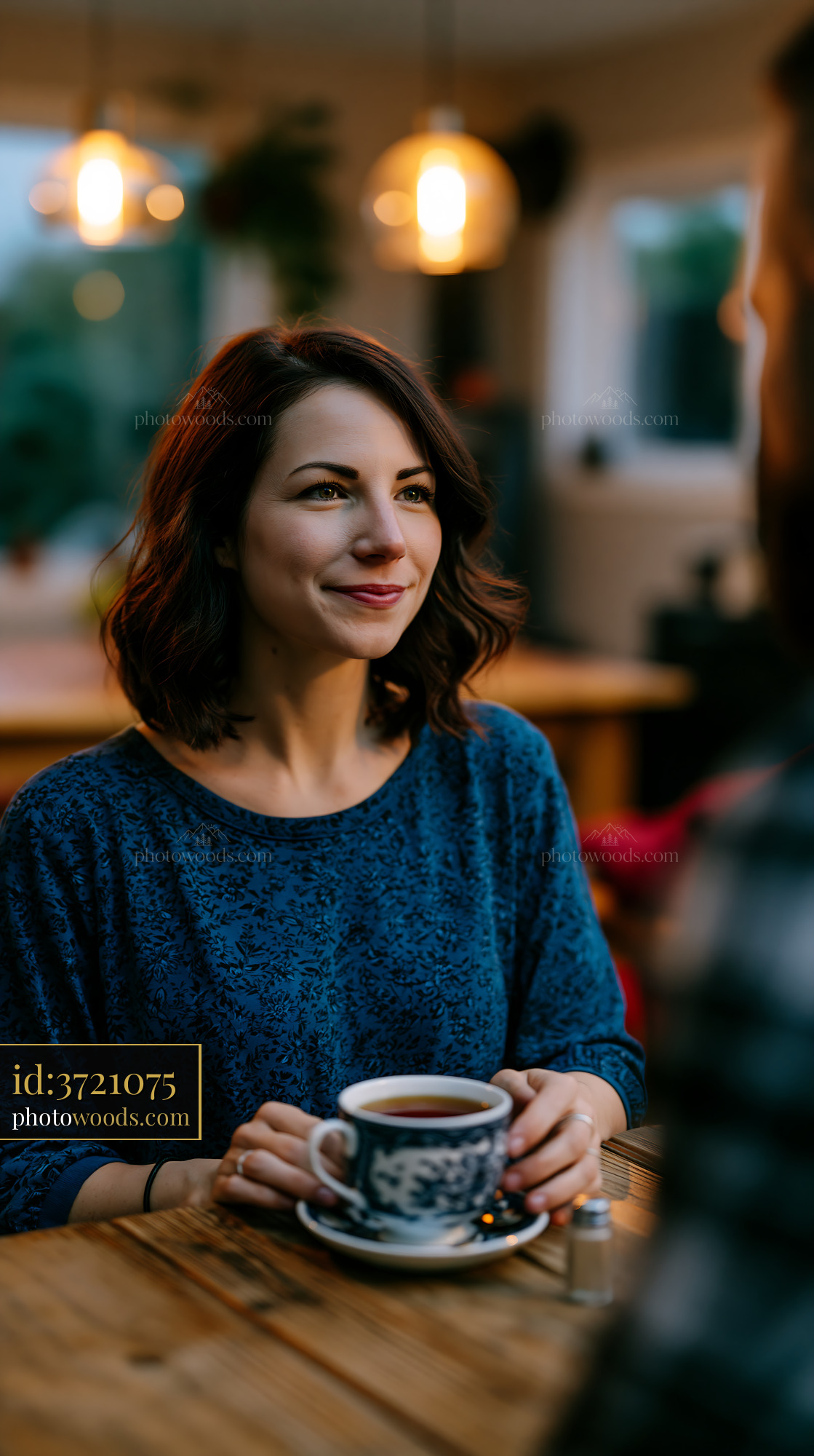 Woman Smiling While Sitting at a Table Holding a Coffee Cup Indoors
