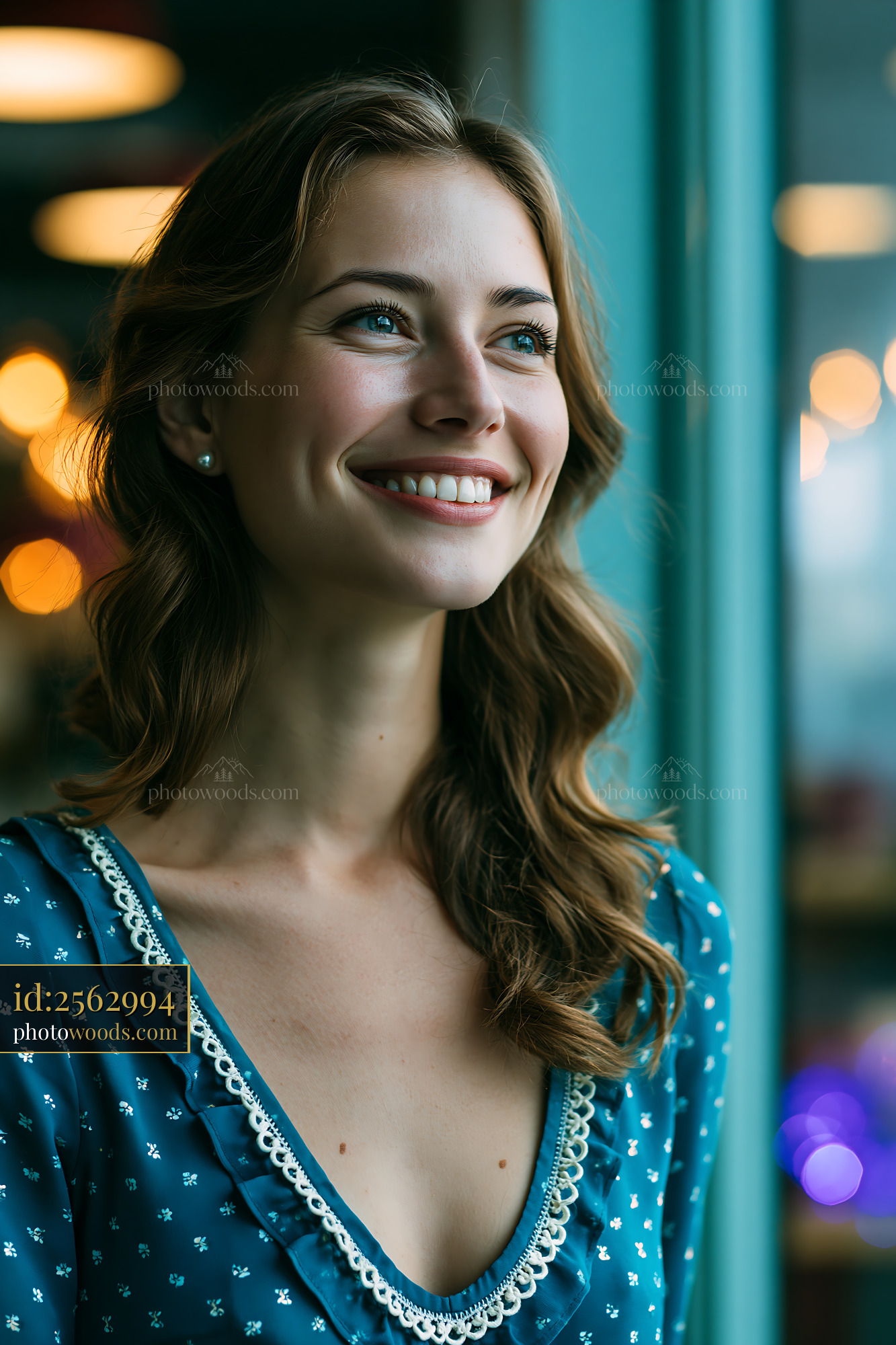 Woman in Blue Dress Smiling Indoors With Warm Lights in Background